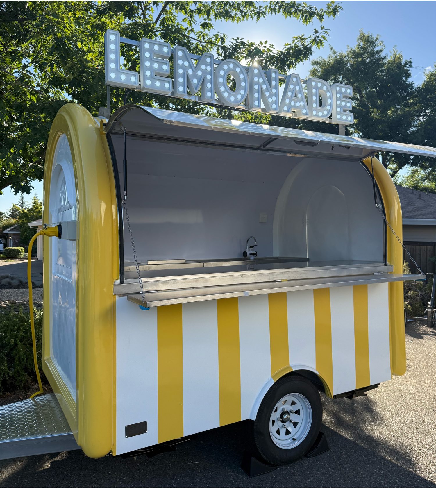 The Citrus Society lemonade trailer, yellow and white striped with an illuminated LEMONADE marquee sign